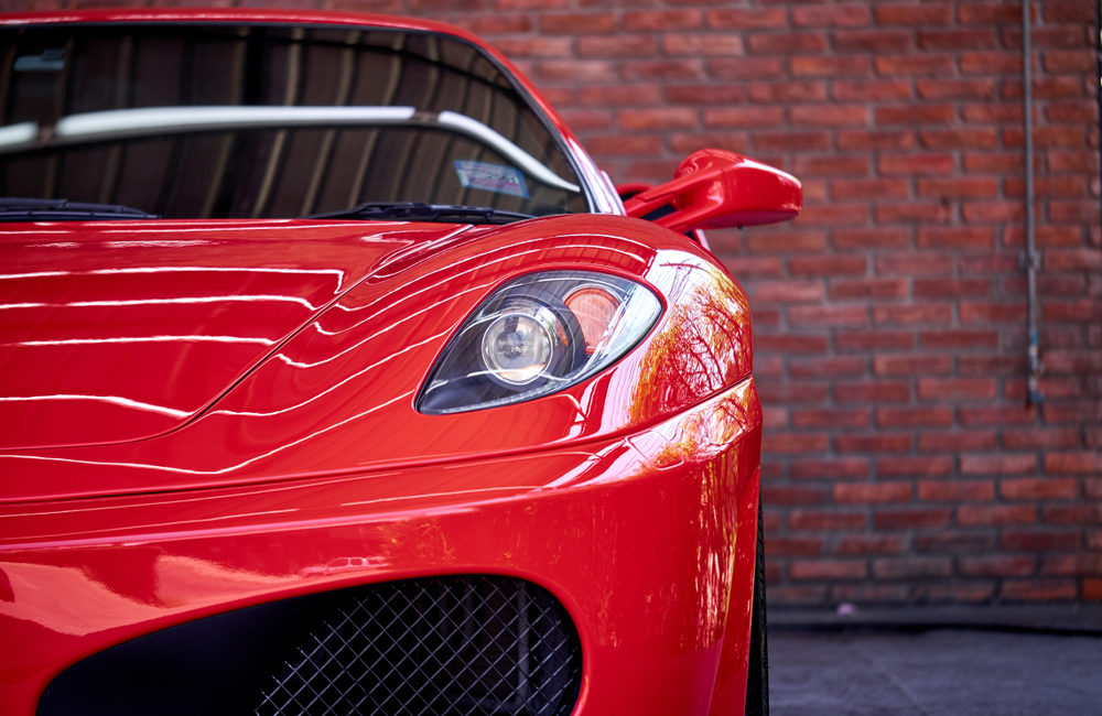 How to Safely Ship Your Classic Car Across the Country Close up of headlight detail of modern luxury sportscar with reflection on red paint after wash & wax. Front view of supercar with brick wall. Concept of car detailing and paint protection background.