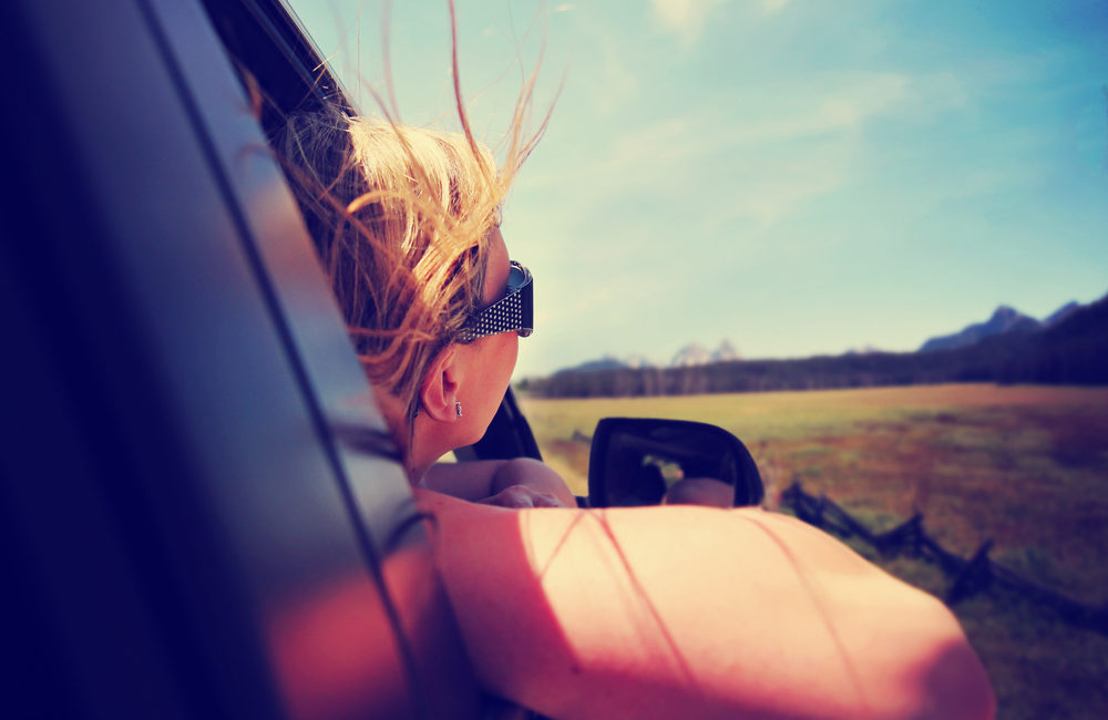A Beginner’s Guide to Transporting Vehicles Across the Country - a woman with her head out the window enjoying a scenic drive